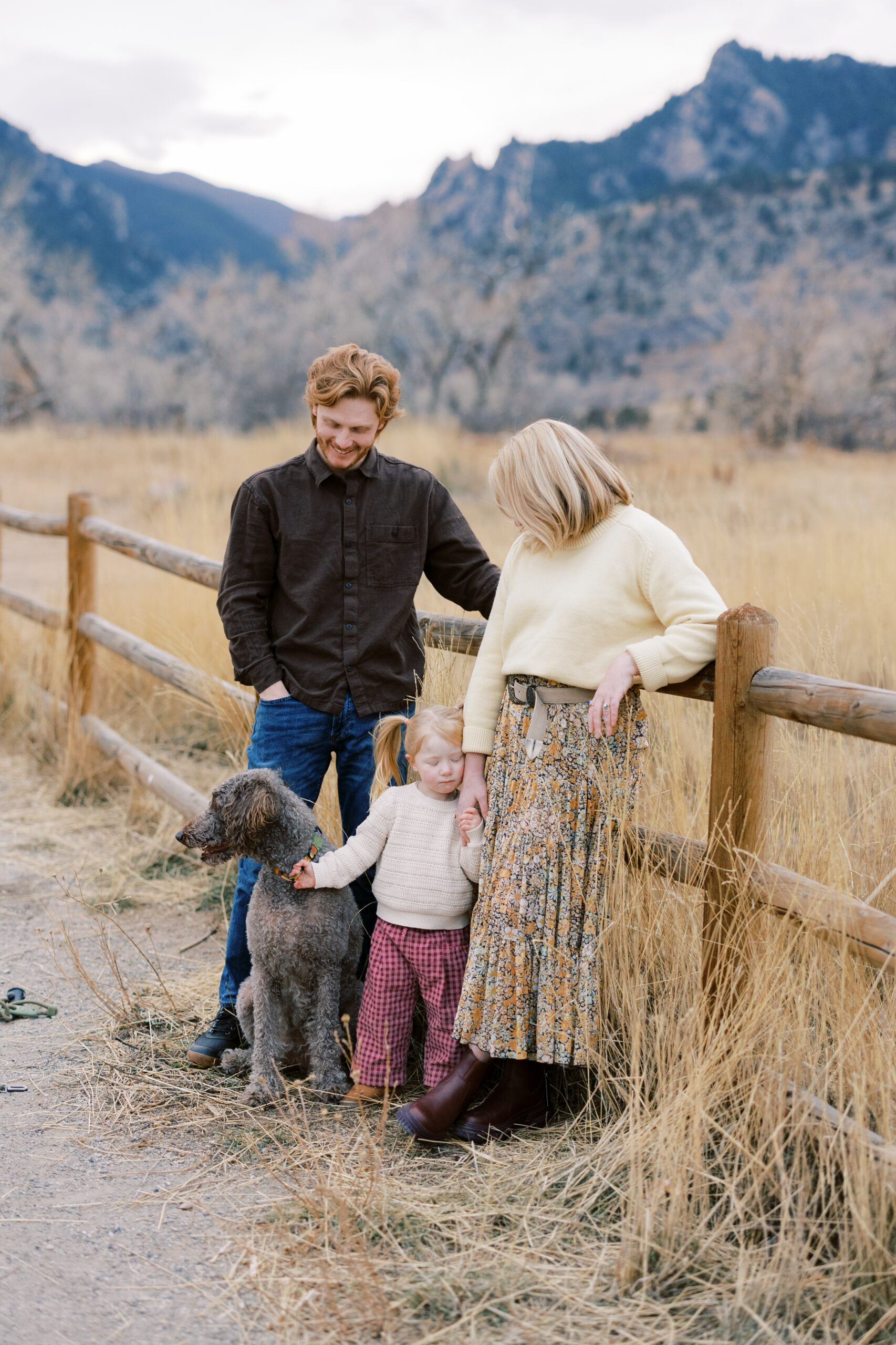 Candid family moment in tall grass with mountains behind them at South Boulder Peak Trailhead in Boulder.