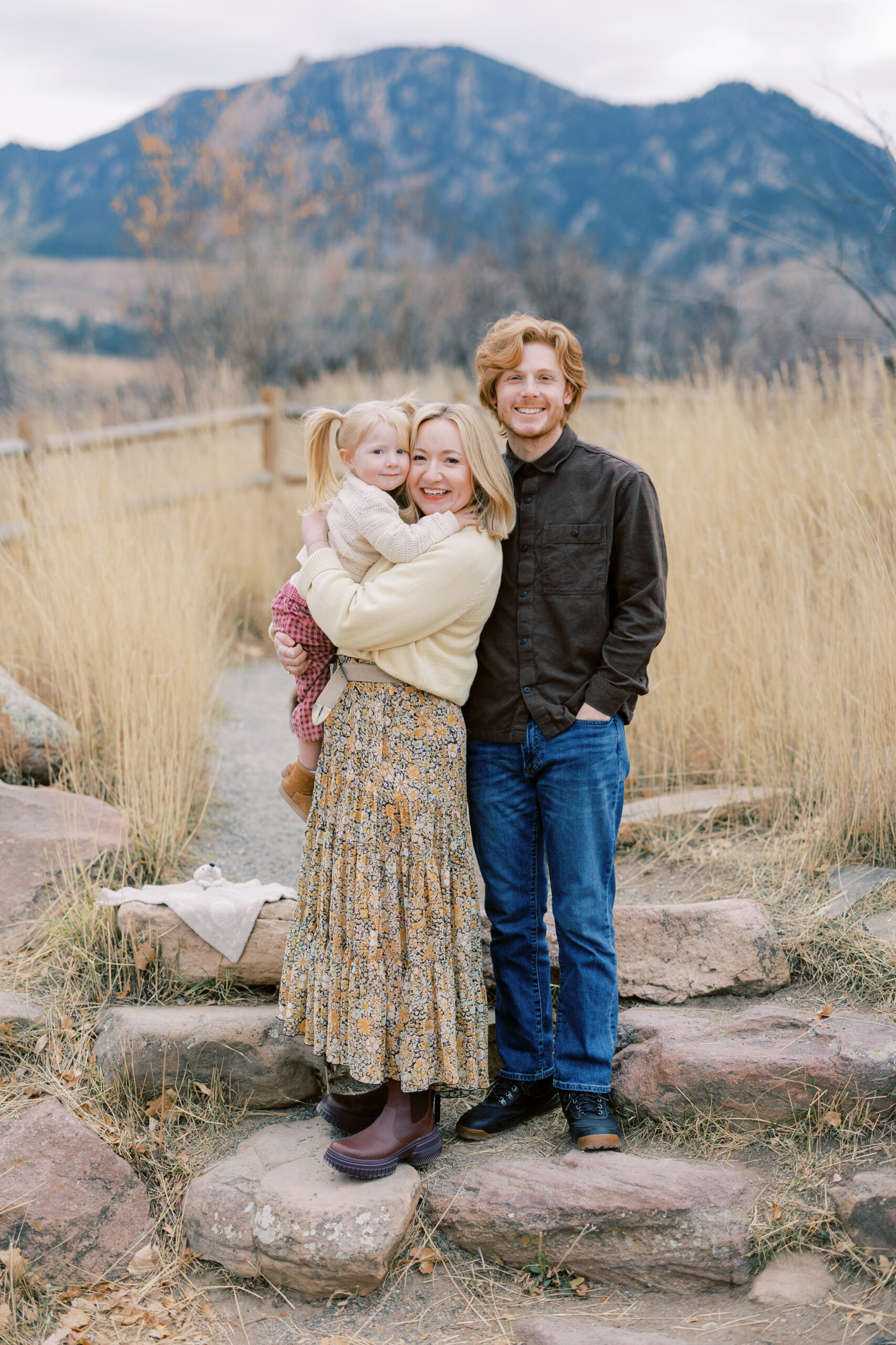 A family of three standing on steps in front of the flatirons of colorado
